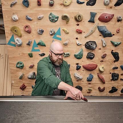 Bild von Lexware: Handwerker arbeitet konzentriert an einem Werkst&uuml;ck in seiner Werkstatt vor einer Kletterwand.