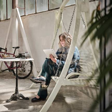 Eine Frau auf einer Hollywood-Schaukel, die ein Tablet bedient.