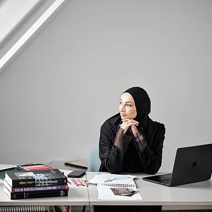 Bild von Lexware: Eine Unternehmerin sitzt am Schreibtisch vor ihrem Laptop und schaut nachdenklich aus dem Fenster