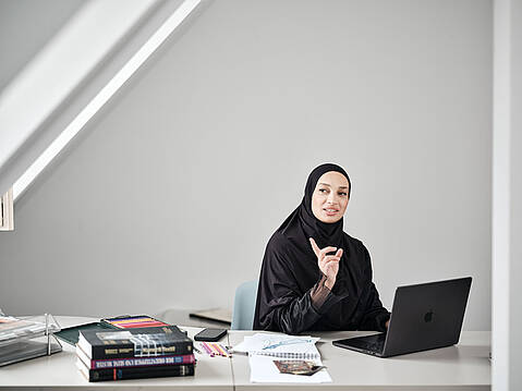 Bild von Lexware: Frau sitzt mit erhobenem Zeigefinger am Schreibtisch vorm Laptop