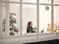 Bild von Lexware: Sicht von au&szlig;en durchs Fenster auf eine Unternehmerin am Schreibtisch vorm Bildschirm