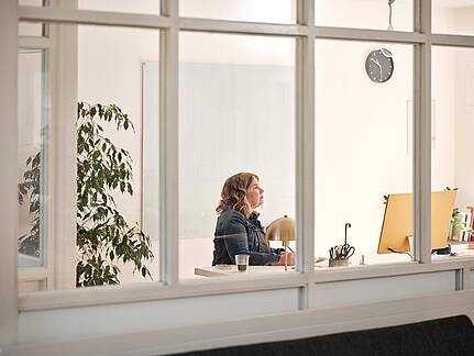 Bild von Lexware: Sicht von au&szlig;en durchs Fenster auf eine Unternehmerin am Schreibtisch vorm Bildschirm