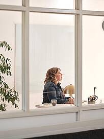 Bild von Lexware: Sicht von au&szlig;en durchs Fenster auf eine Unternehmerin am Schreibtisch vorm Bildschirm